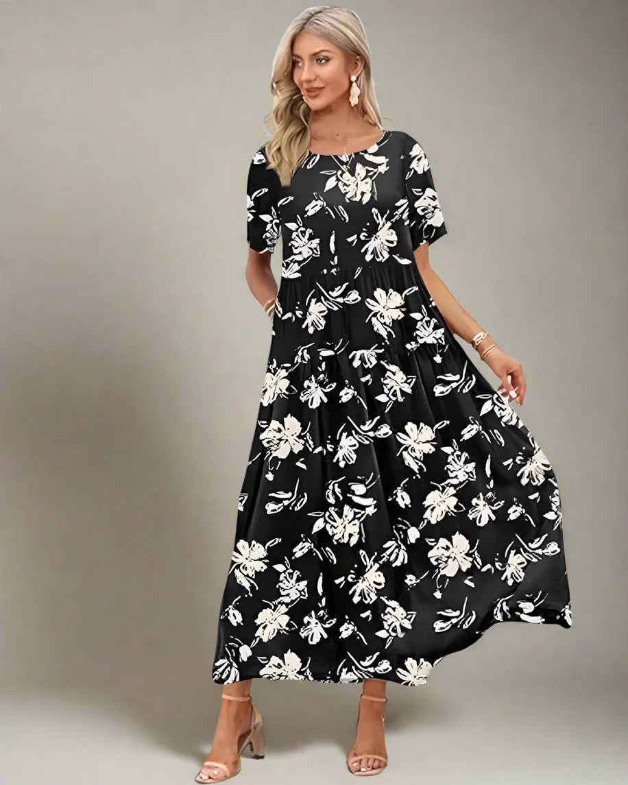 Woman in a black floral dress standing on a wooden deck with palm trees and ocean in the background
