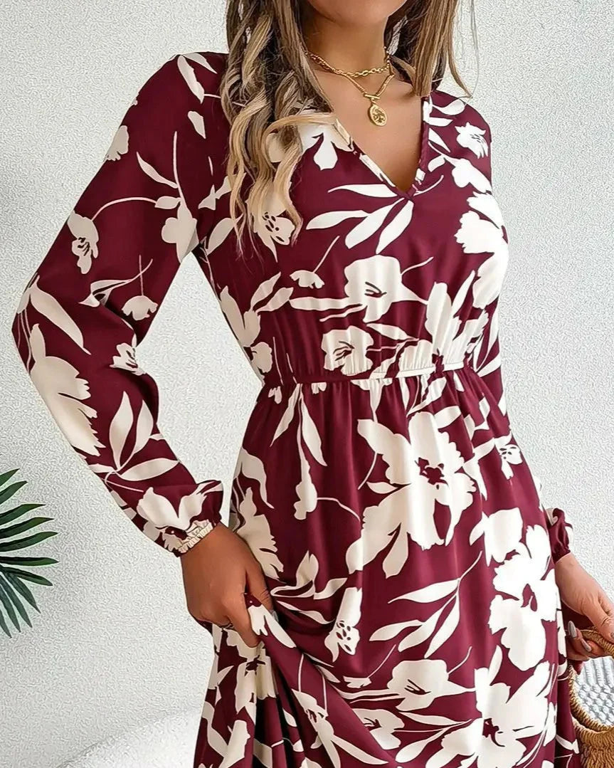 Woman wearing a burgundy and white floral dress holding a straw bag indoors.