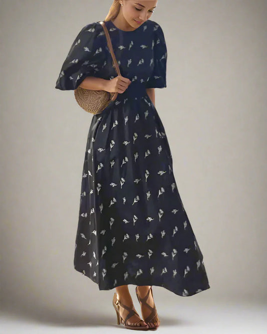 Woman wearing a navy blue dress with white patterns, holding a woven bag on a light background
